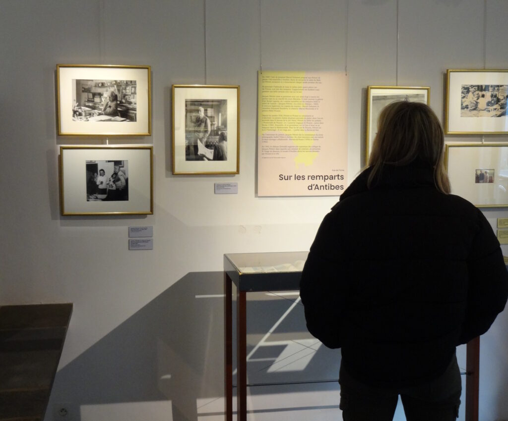 Une visiteuse observe des photographies dans l'exposition temporaire. Le panneau sur le mur devant elle indique "Sur les remparts d'Antibes".