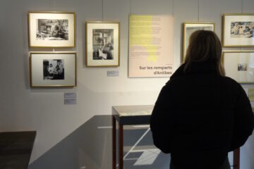 Une visiteuse observe des photographies dans l'exposition temporaire. Le panneau sur le mur devant elle indique "Sur les remparts d'Antibes".