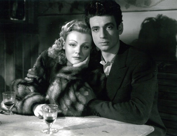 Nathalie Nattier et Yves Montand assis à une table dans le film Les Portes de la nuit