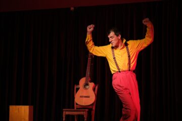 Un homme danse avec les bras levés. A côté de lui, une guitare est posée sur une chaise.