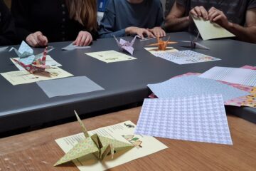 Sur une table sont posées des feuilles et des origamis.