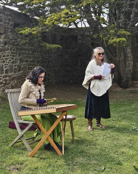 Deux femmes sont dans un jardin. Celle à gauche est assise et joue du dulcimer, un instrument à cordes. Celle à droite est debout, elle lit des poèmes.