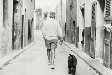 Jacques Prévert de dos marche dans une rue en tenant son chien à la laisse