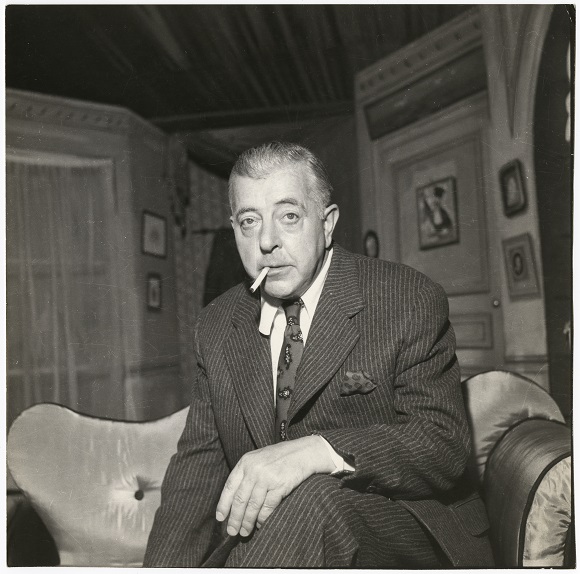 Jacques Prévert est assis sur un canapé dans un décor de théâtre